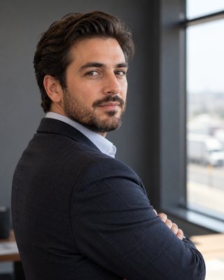 A portrait of a professional working in founder of a regional freight brokerage, from the chest up, turned away and looking back over the shoulder, against a cool grey wall.