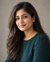 A woman in her thirties with long dark hair, in a dark teal top, photographed from the chest up against a plain warm neutral background.